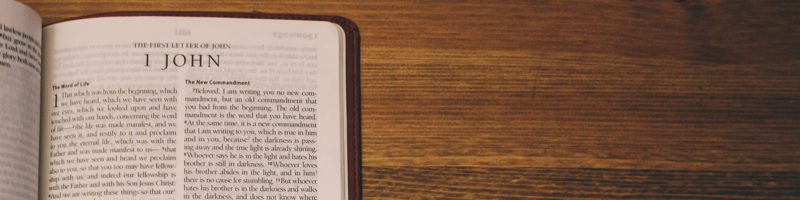 open bible on wood table showing the book of 1 john in the new testament