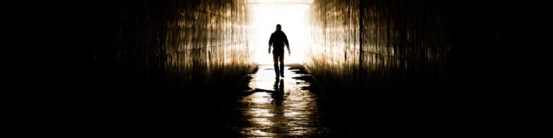 photo of man walking into a dark tunnel with bright light behind him